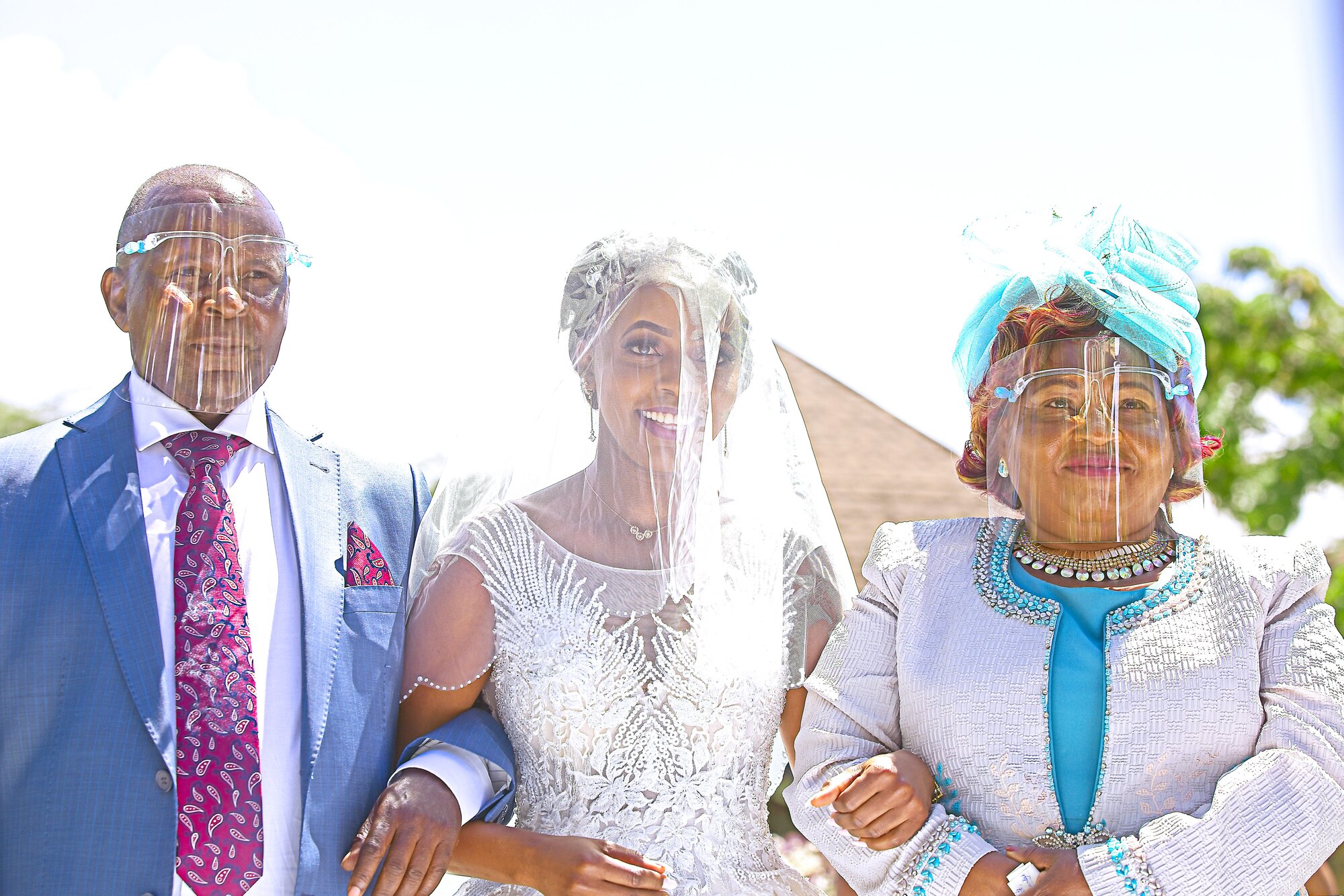 A bride is escorted into an outdoor ceremony by two older relatives.