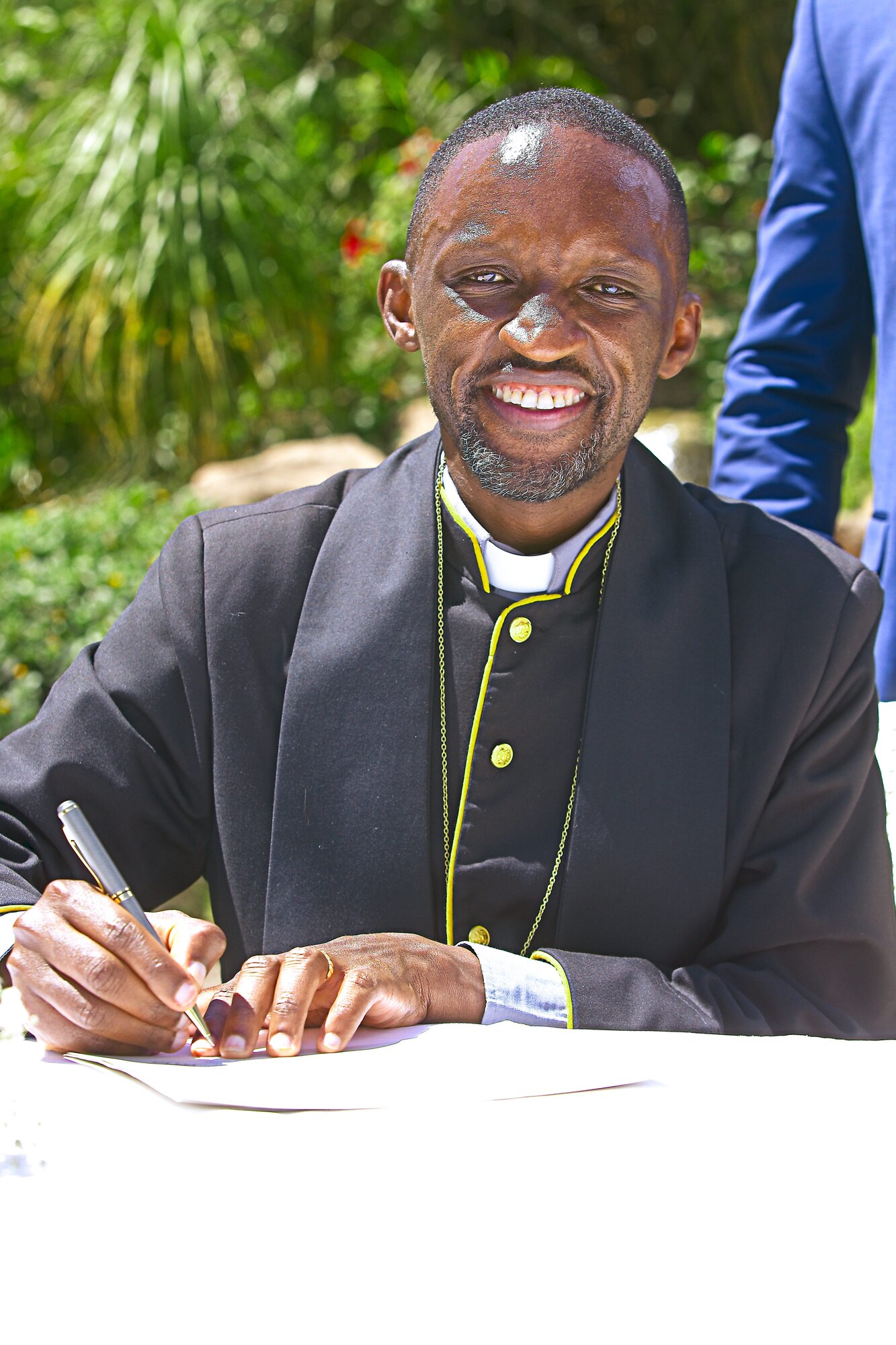 An officiant smiles while signing a document at the ceremony table.